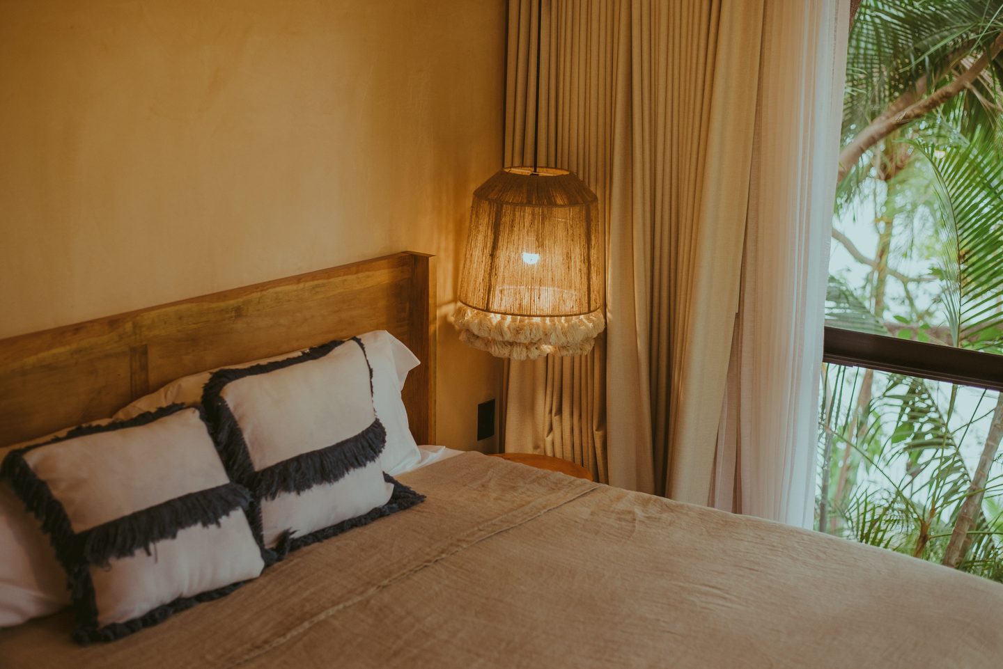 Cama con cabecero de madera y lámpara de fibra encendida junto a la ventana